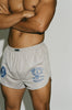 Close-up of a shirtless muscular male model wearing Y,IWO x Ace Hotel grey microfiber quad shorts with blue bodybuilding graphics, short inseam, and curved side hems that expose the thighs.