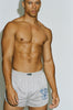 Muscular shirtless male model wearing Y,IWO x Ace Hotel grey short-inseam gym shorts featuring blue strongman artwork, a relaxed athletic fit, and curved hems that highlight muscular legs.
