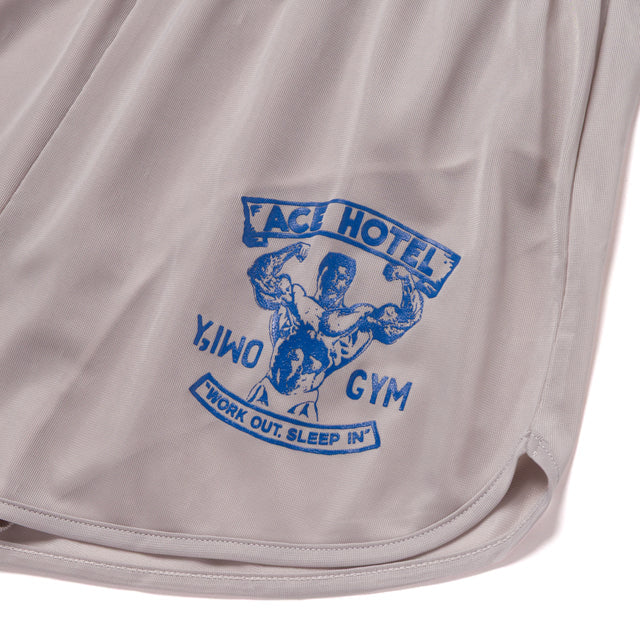 Close-up of Y,IWO x Ace Hotel grey quad shorts featuring blue vintage bodybuilding artwork by Ariel Roman, a muscular strongman in a double-biceps pose, Ace Hotel Gym branding, and Work Out, Sleep In slogan.