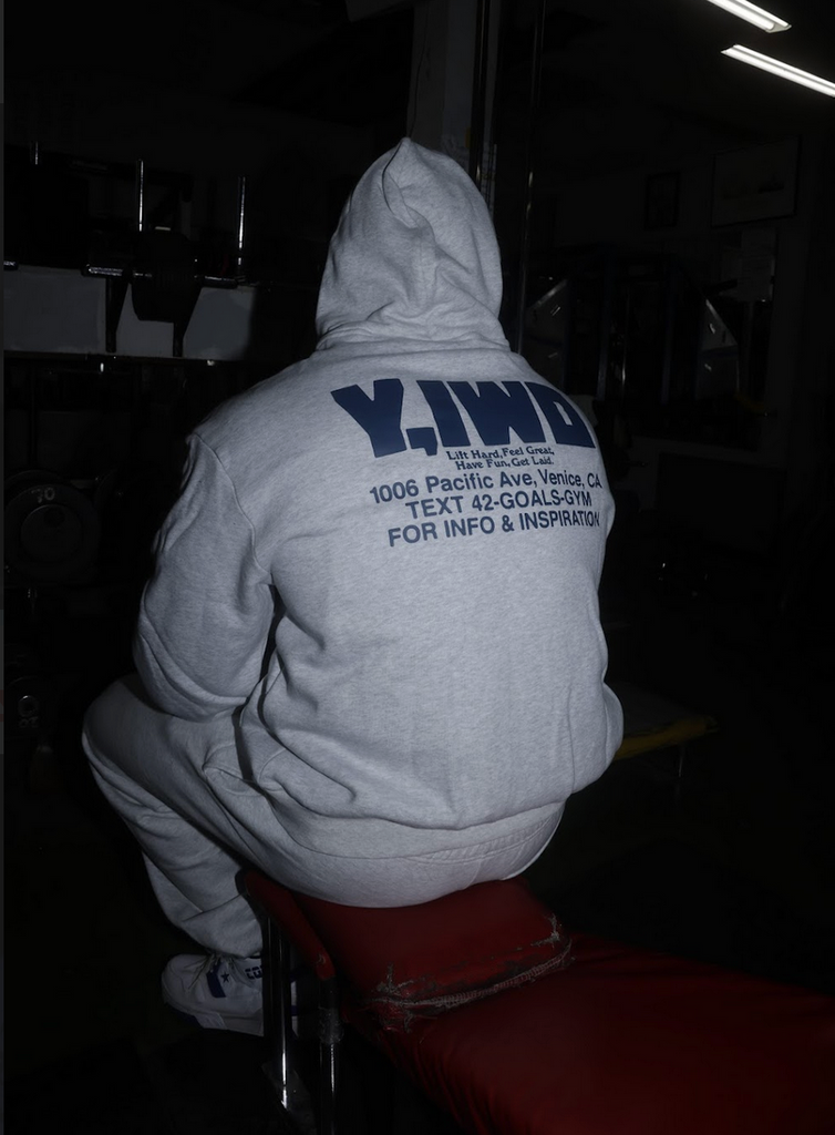 Person wearing a hoodie with text on the back, sitting in a dark room.